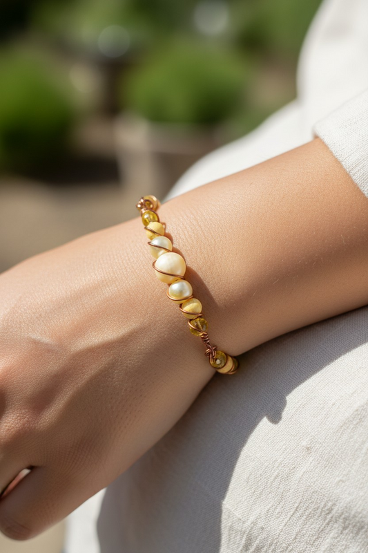 Close-up of a bracelet worn on a wrist in bright sunlight. At the center is a pale yellow jade bead, bracketed by yellow resin pearls, yellow lava beads, and translucent yellow rondelle beads. Copper-colored wire is twisted into orbital spirals around each bead, securing them in place and forming small wrapped sections along the design.