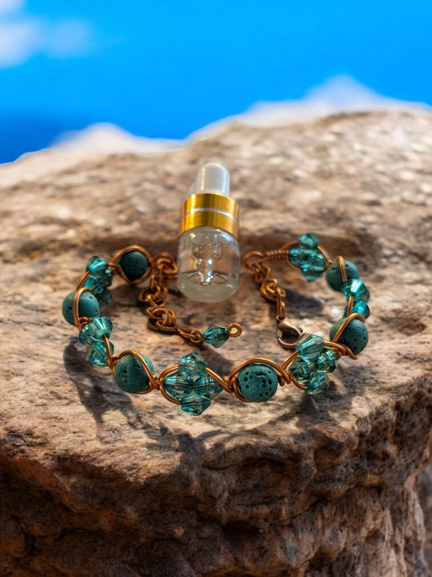 Handcrafted adjustable cuff diffuser bracelet with teal lava stones and teal resin bicone beads wrapped in copper-colored hypoallergenic wire, displayed on a rock with a bright blue sky background.