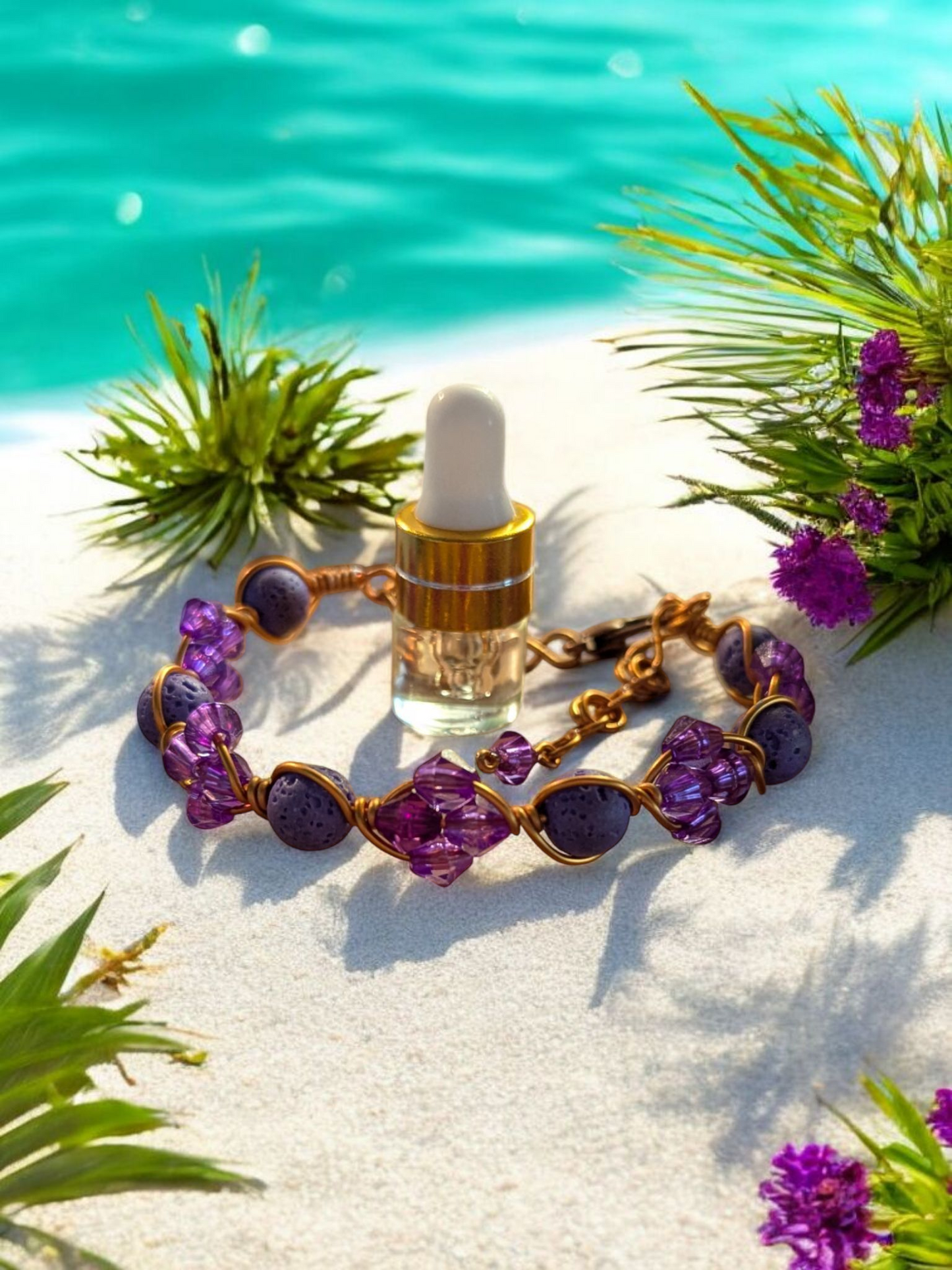 Handcrafted purple diffuser cuff with purple lava beads, resin bicone beads, and copper hypoallergenic wire displayed on white sand near turquoise water and purple flowers.
