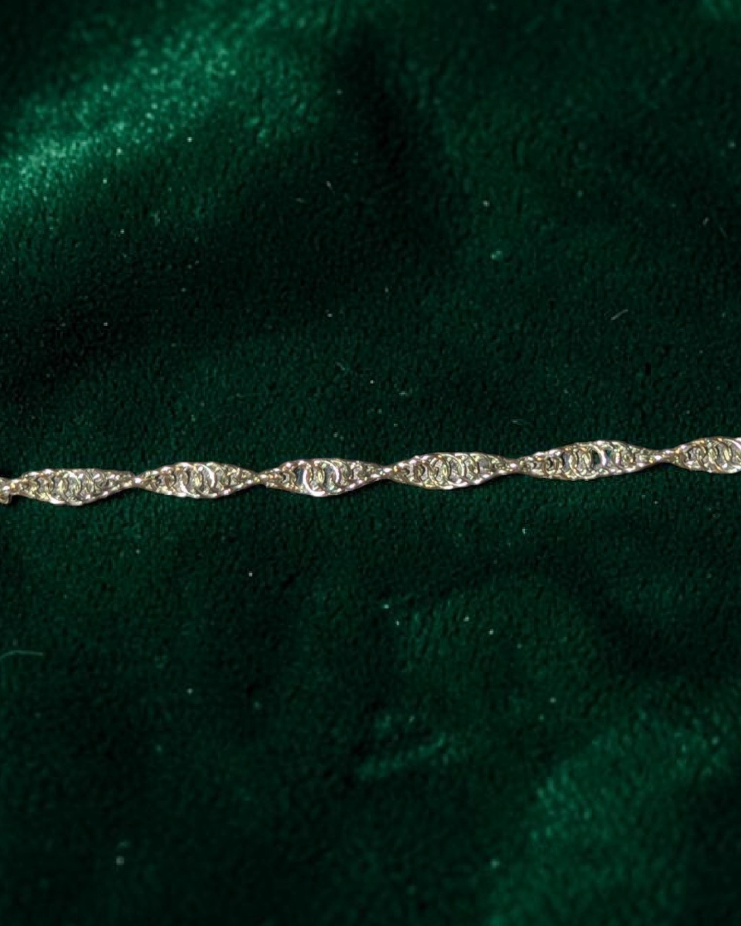 A close-up macro of the Snerill spiral 4-in-1 chainmail bracelet in Pale-Mint, its soft pale silvery-mint aluminum rings twisting in a continuous helix across deep emerald velvet.