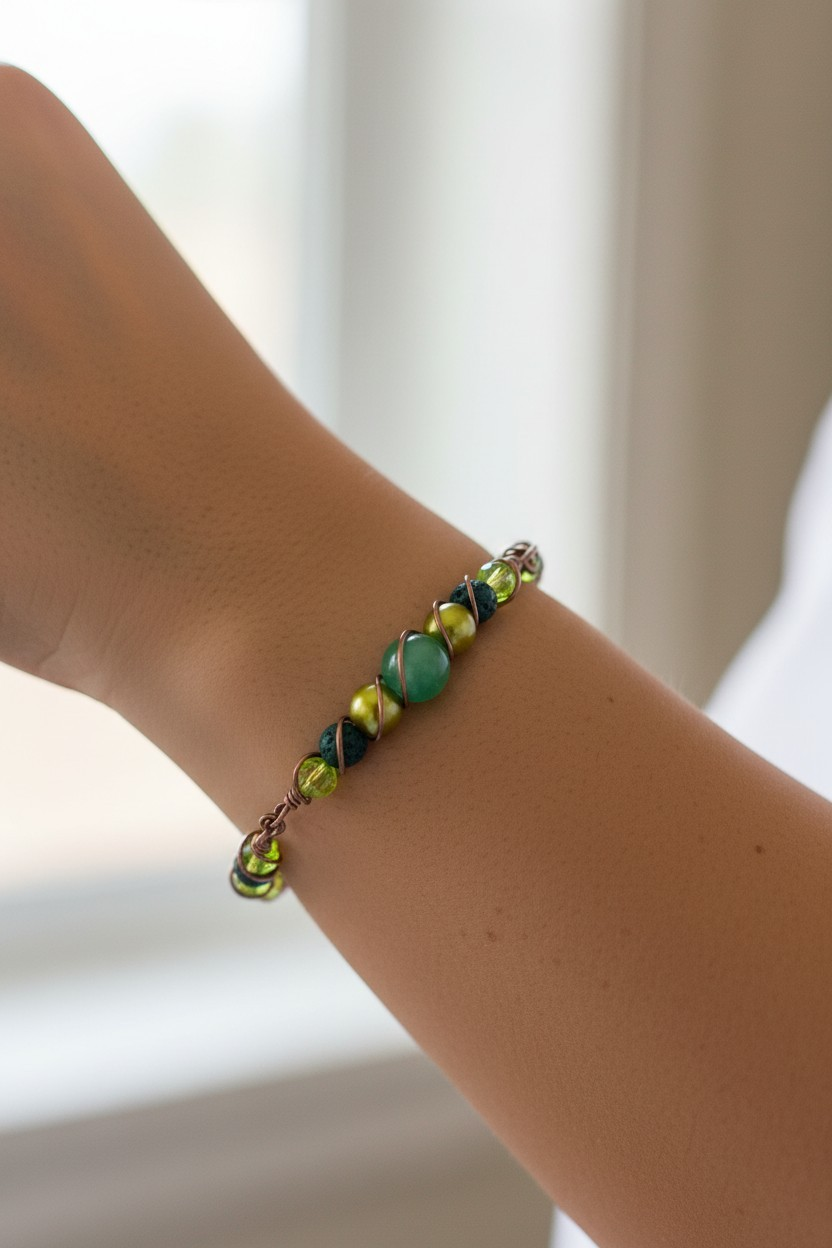 Close-up of a bracelet worn on a wrist, featuring a central green aventurine bead flanked by glossy green resin pearls, dark green lava beads, and translucent lime-green bicone beads. Twisted spiral antique brass–colored wire wraps around the beads, holding them securely in place and forming small coiled ends at each side.