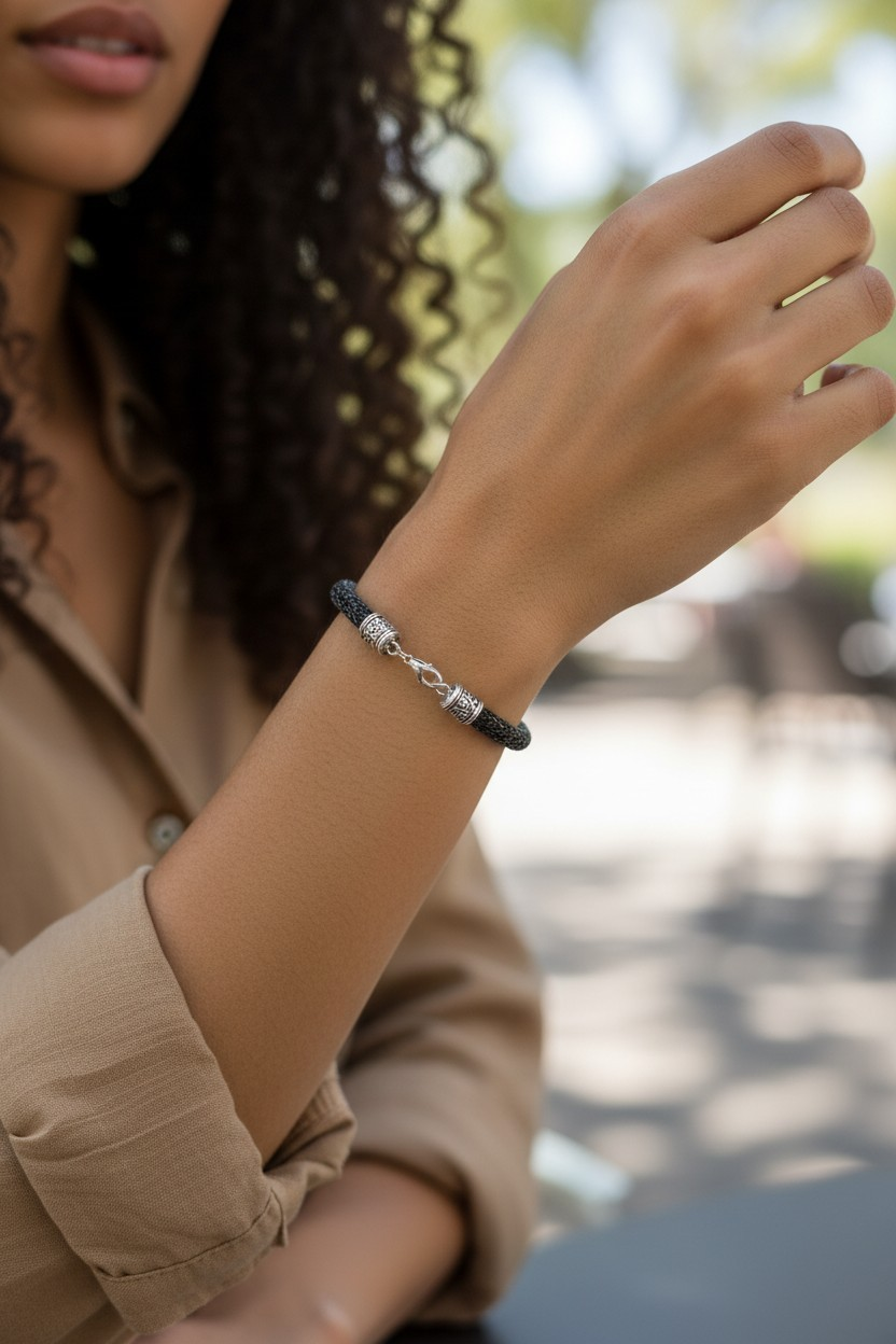 A model wearing a Viking knit bracelet made from distressed black lacquered copper wire. The woven wire forms a circular band around the wrist and is finished with antique silver Tibetan-style end caps and a silver lobster clasp. The bracelet is shown outdoors with the model’s arm slightly raised, highlighting the texture of the woven metal and the contrast between the dark knit wire and the silver fittings.