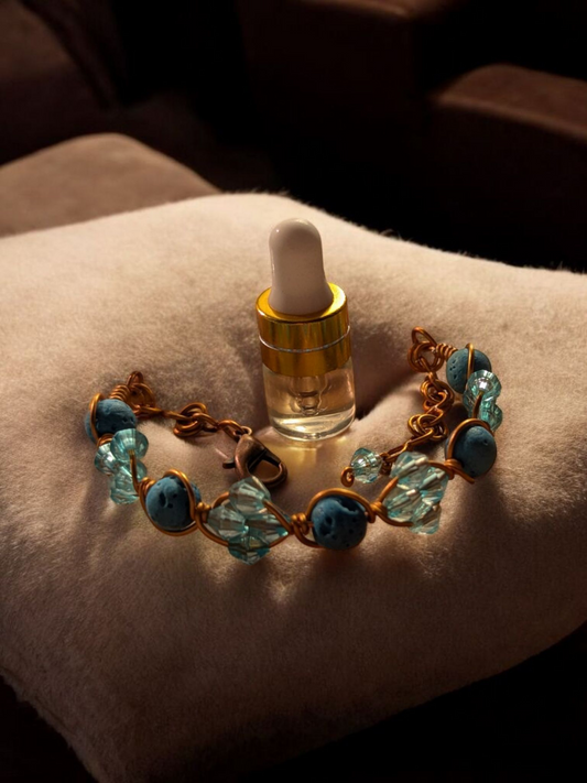 Handcrafted adjustable cuff diffuser bracelet with aqua lava stones and light aqua resin bicone beads wrapped in copper-colored hypoallergenic wire, displayed on a cream-colored cushion.