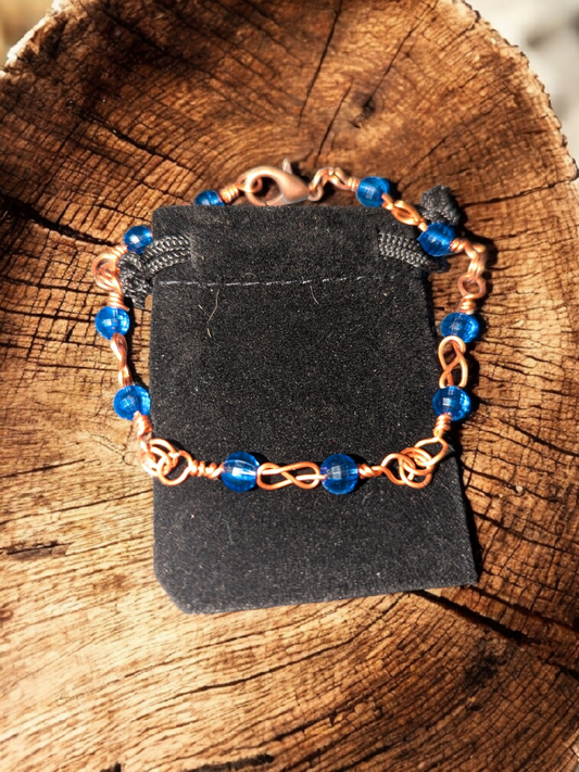 Copper wire love-knot bracelet with bright blue beads displayed on a tree stump.