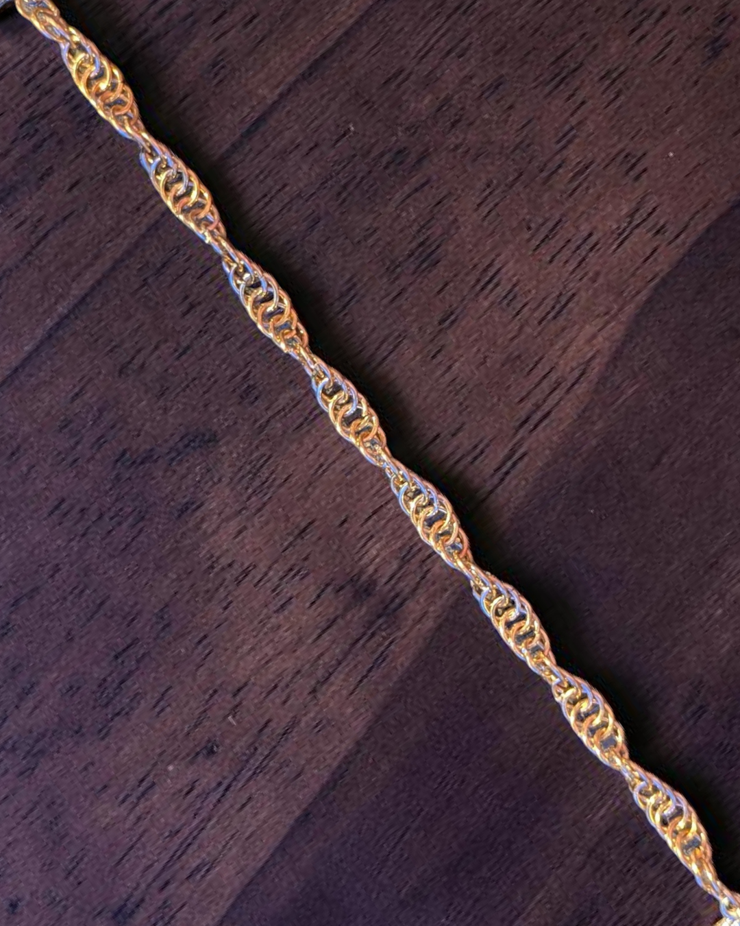 A close-up macro of the Snerill spiral 4-in-1 chainmail bracelet in Champagne, its warm golden aluminum rings twisting in a continuous helix across rich dark wood grain.