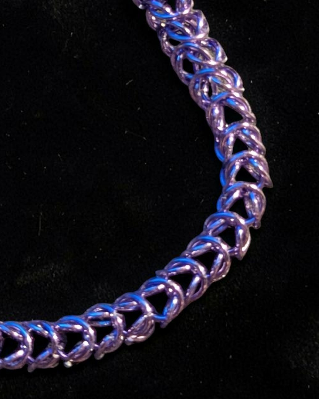 A close-up macro of the Brikk box weave chainmail bracelet in Lilac, its cool lavender-purple aluminum rings densely interlocked in the structural box weave pattern across black velvet, with blue highlights catching the light.