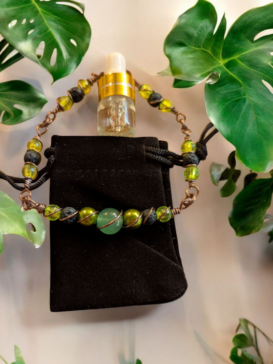 Handcrafted green aventurine diffuser bracelet with dark green lava beads, gold-green resin pearls, lime resin accents, and weathered bronze hypoallergenic wire, displayed on a black velvet pouch surrounded by tropical leaves.