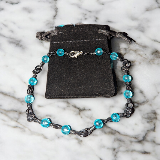 Close-up bracelet photo on marble showing black-colored wire twisted into a love-knot chain with icy aqua colored beads.