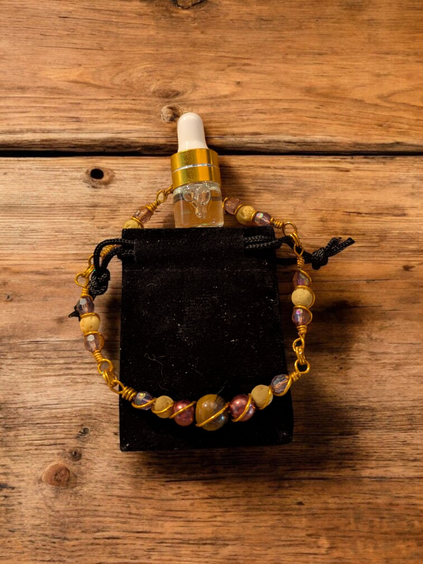 Handcrafted Tiger’s Eye diffuser bracelet with yellow lava stones, bronze resin pearls, and brassy gold hypoallergenic wire, displayed on a black velvet pouch on a wooden surface.