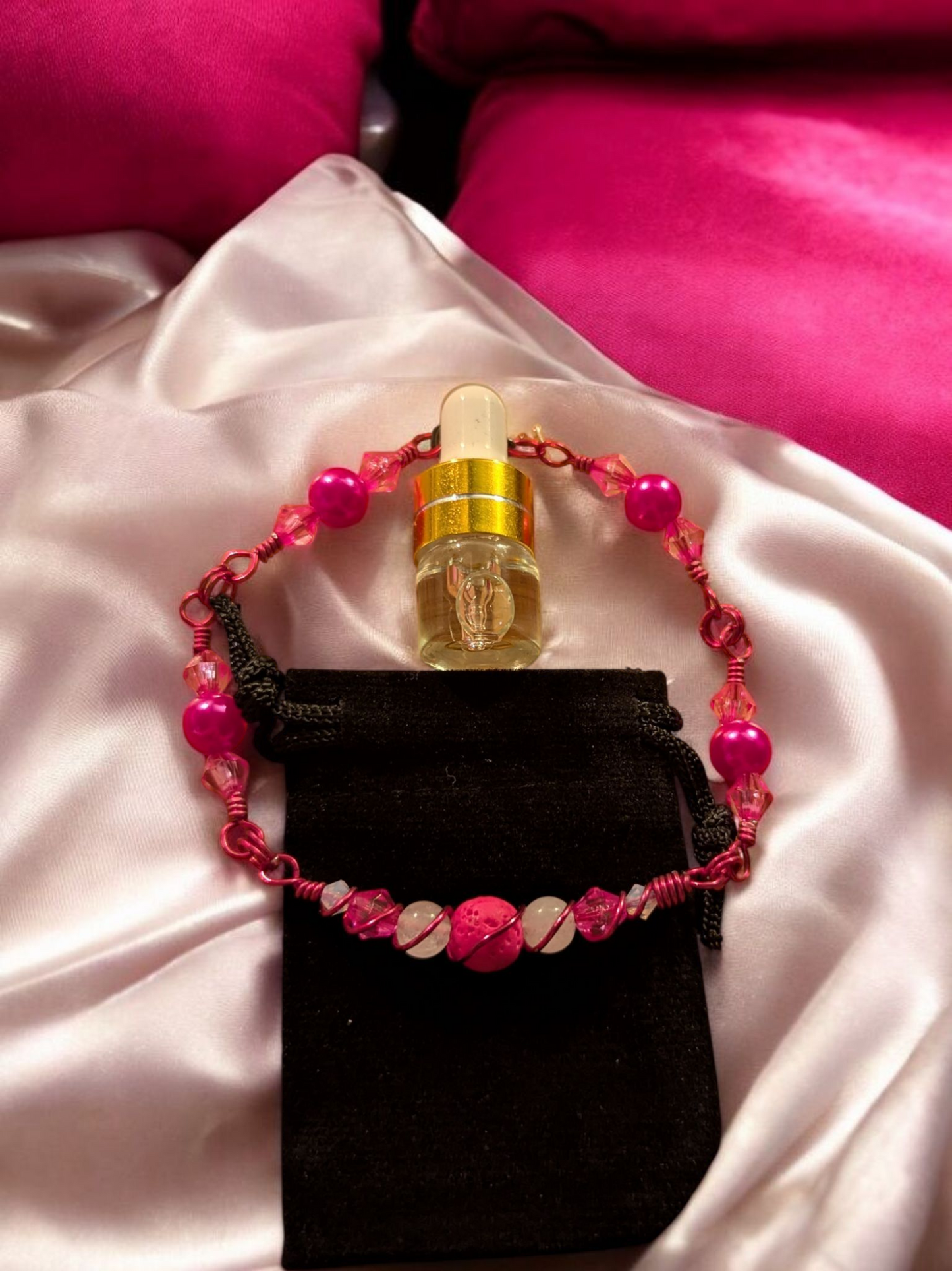Handcrafted pink lava diffuser bracelet with white jade beads, pink resin accents, and pink hypoallergenic wire, displayed on a black velvet pouch atop soft pink satin.