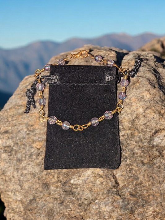 Bracelet on a rock with gold love-knot chain and lavender-gray faceted beads.