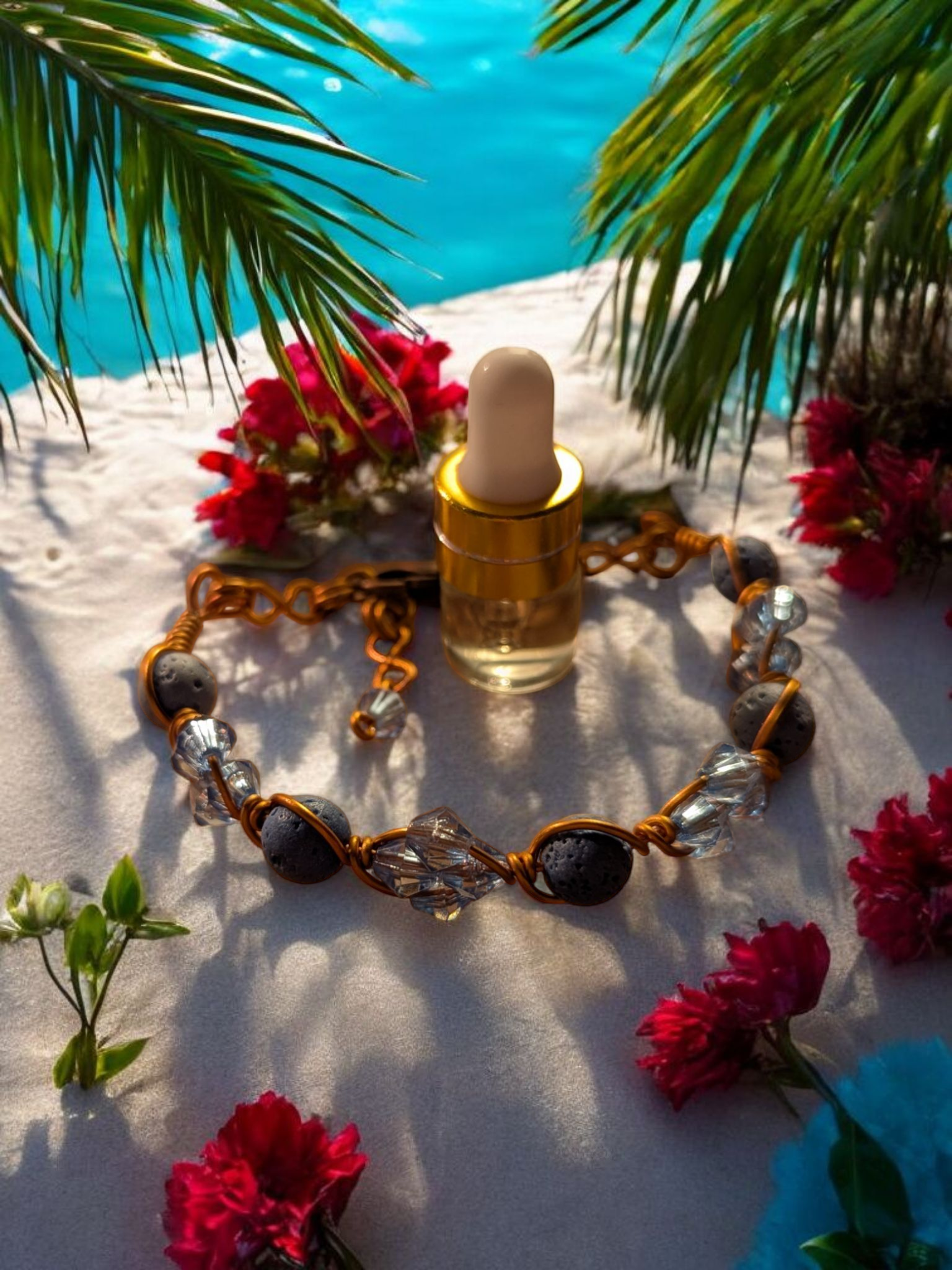 Handcrafted adjustable cuff diffuser bracelet with blue-gray lava stones and light blue resin bicone beads wrapped in copper-colored hypoallergenic wire, displayed on sand beside tropical flowers and palm leaves with a pool in the background.