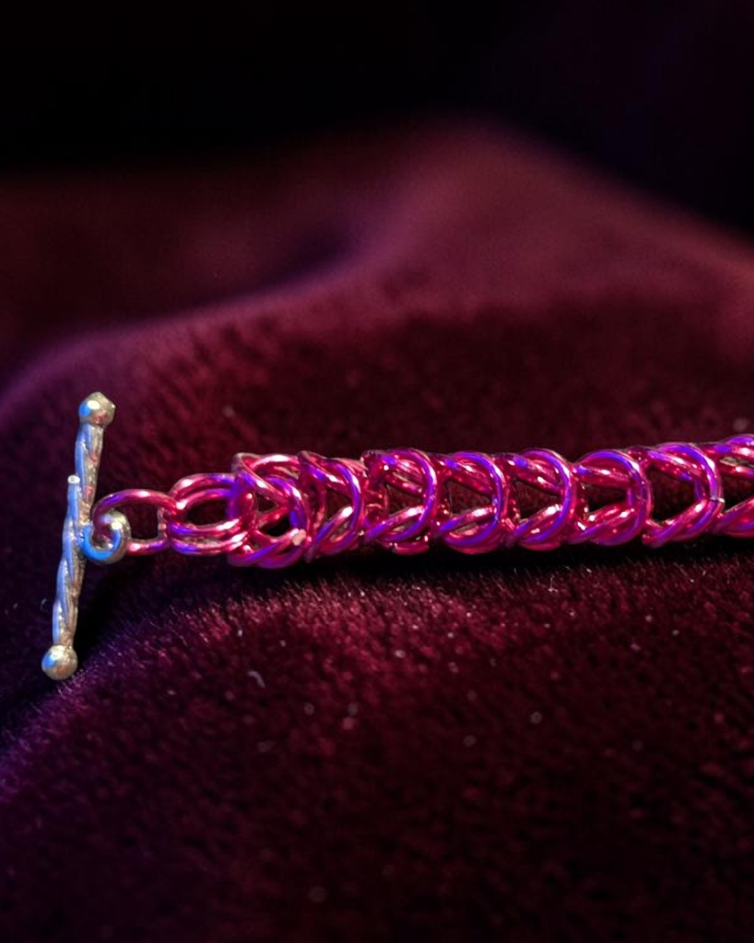A close-up macro of the Brikk box weave chainmail bracelet in Fuchsia, its vivid hot pink aluminum rings densely interlocked in the structural box weave pattern across deep burgundy velvet, with the silver toggle bar clasp visible at the left.