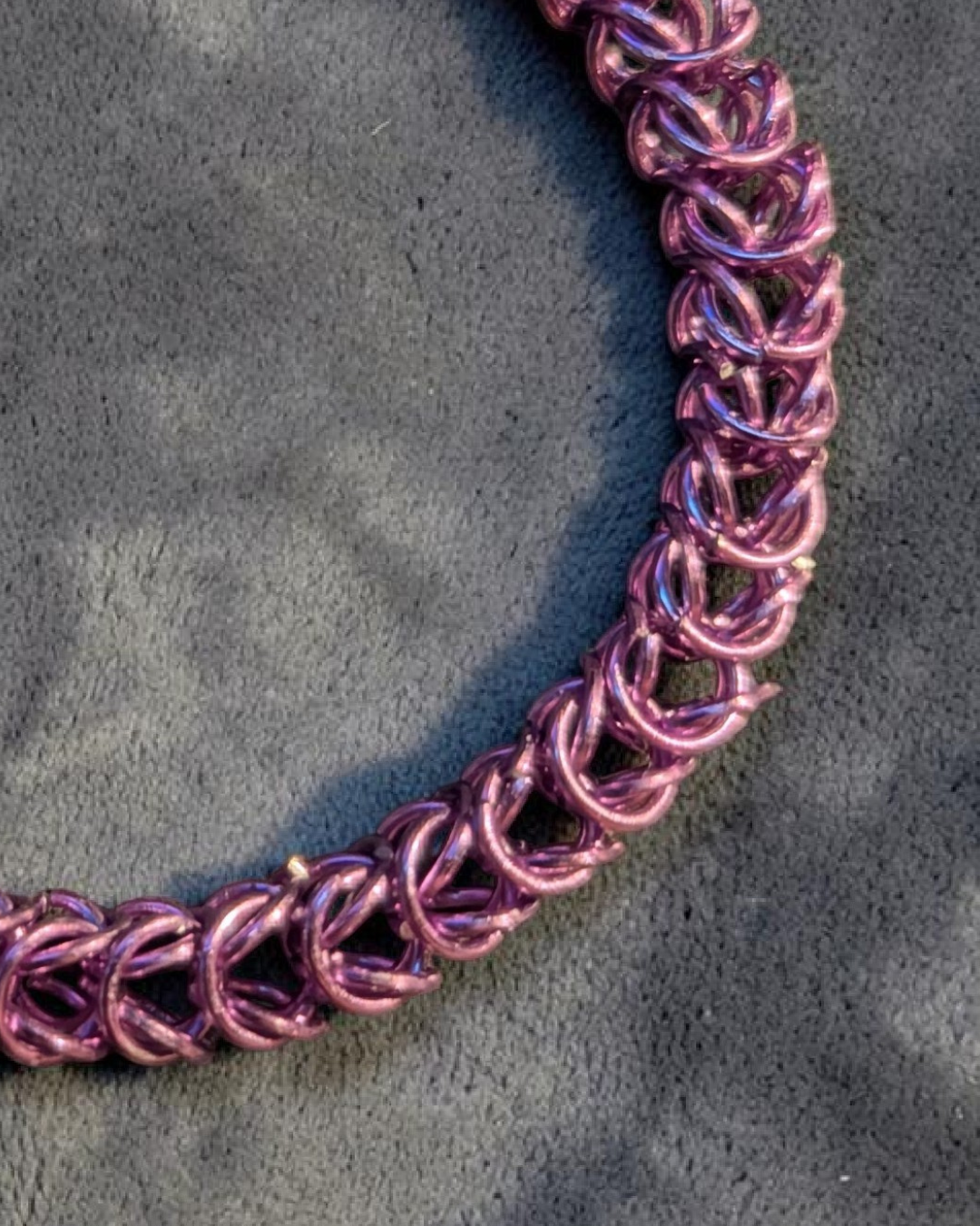 A close-up macro of the Brikk box weave chainmail bracelet in Lavender, its soft pinkish-lavender aluminum rings densely interlocked in the structural box weave pattern on a gray velvet surface.