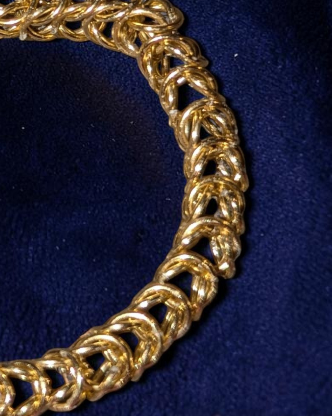 A close-up macro of the Brikk box weave chainmail bracelet in Pale-Gold, its warm yellow-gold aluminum rings densely interlocked in the structural box weave pattern across deep navy velvet.