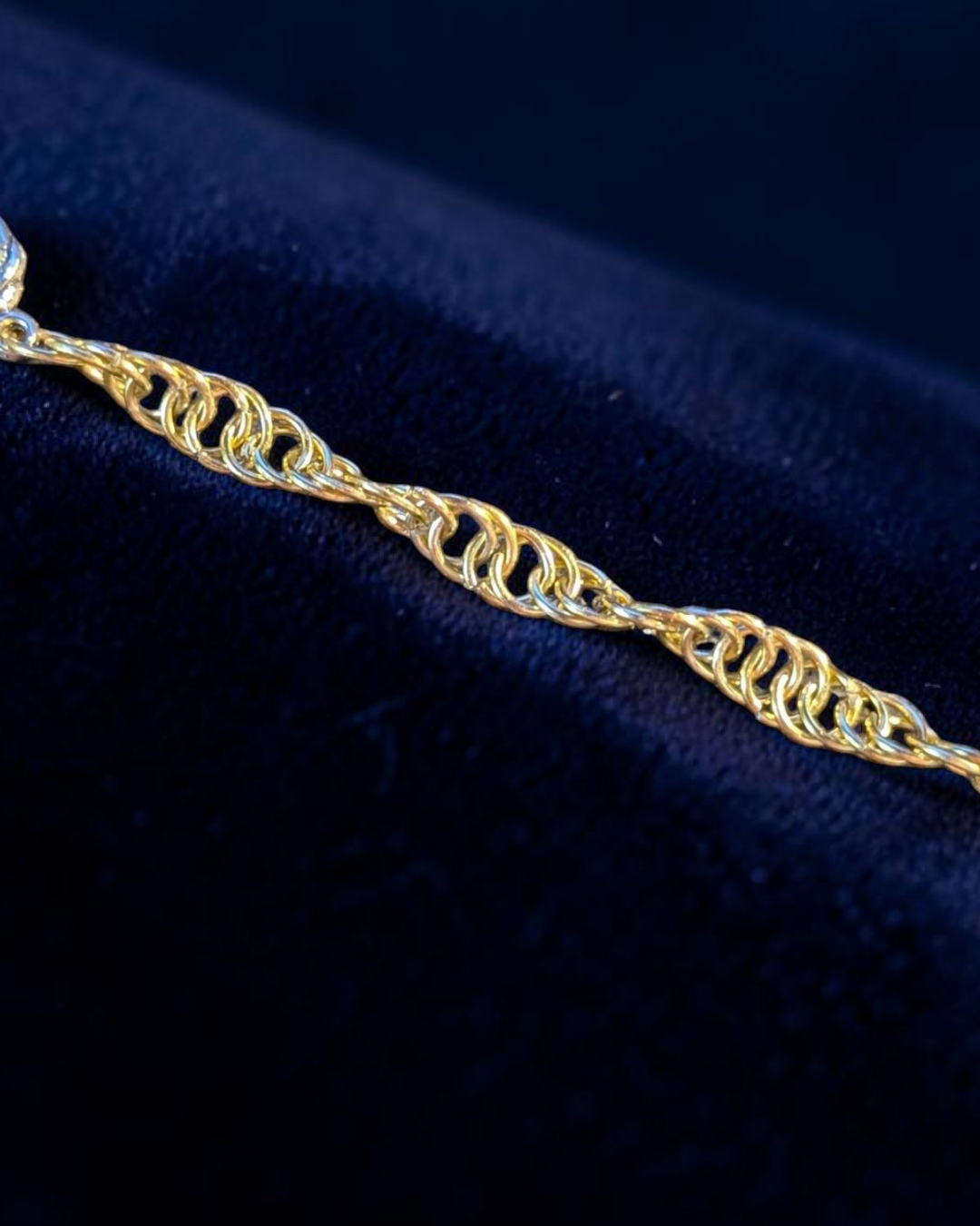 A close-up macro of the Snerill spiral 4-in-1 chainmail bracelet in Pale-Gold, its soft yellow-gold aluminum rings twisting in a continuous helix across deep navy velvet.