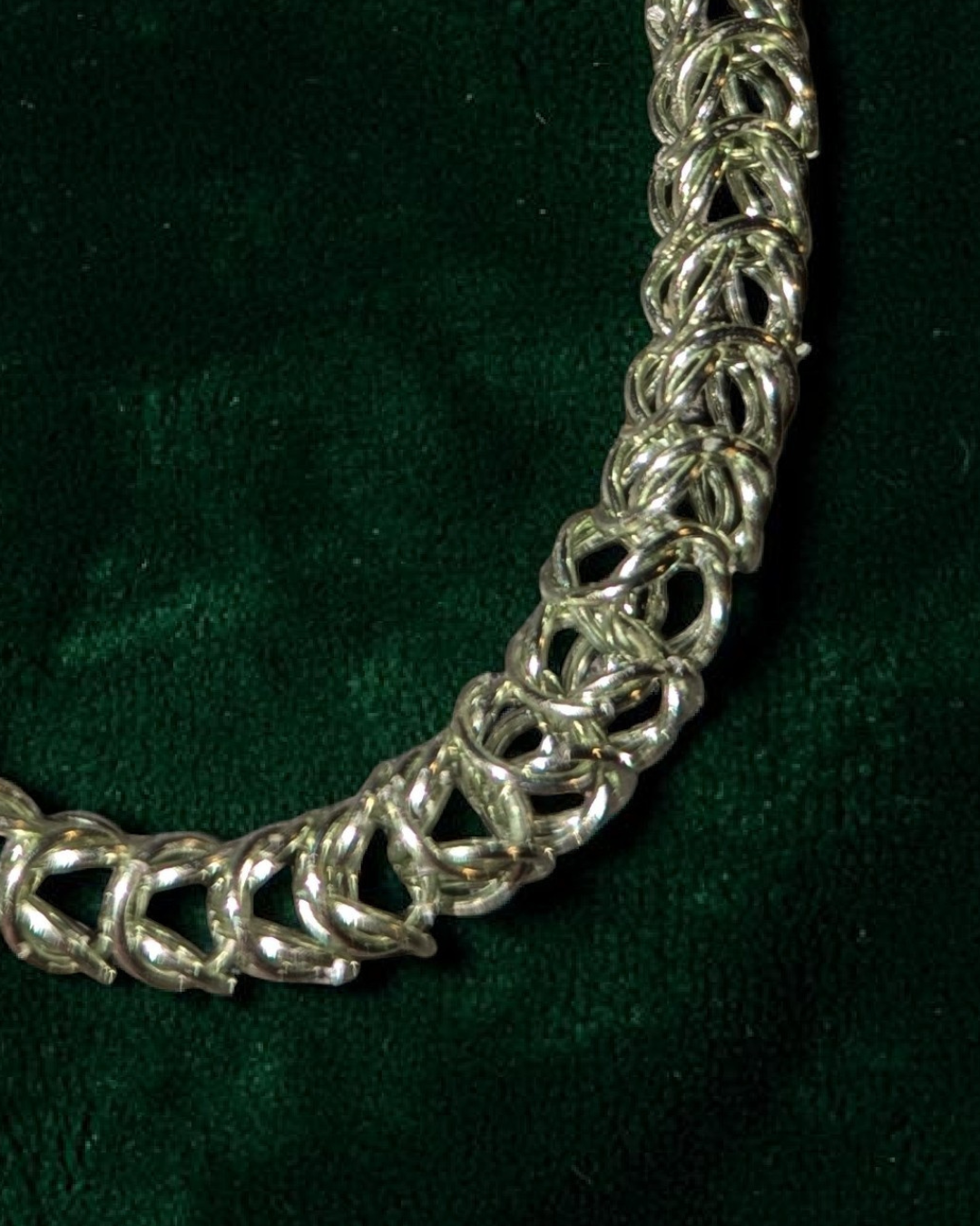 A close-up macro of the Brikk box weave chainmail bracelet in Pale-Mint, its soft silvery-mint aluminum rings densely interlocked in the structural box weave pattern across deep emerald velvet.